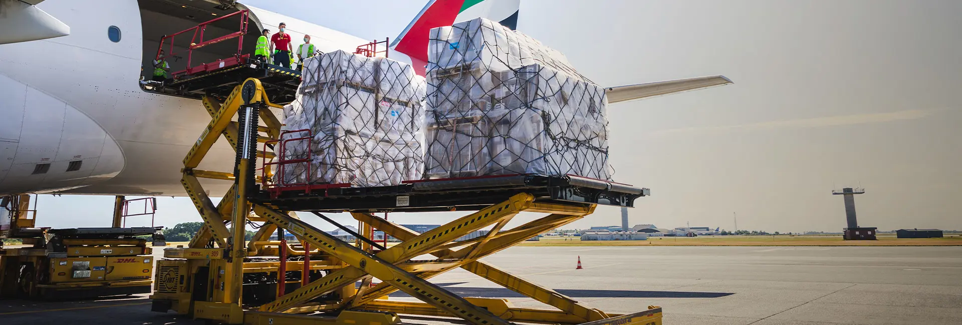 Cargo pallets being loaded into the hold of an Emirates SkyCargo plane using a hydraulic loader on the airport tarmac.