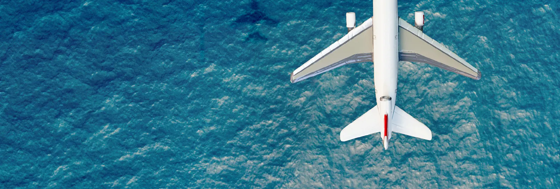 Top-down view of a white airplane flying over a vast blue ocean