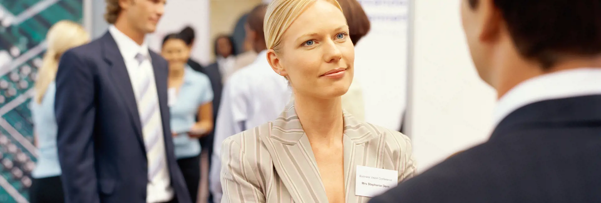 Businesswoman in a striped suit networking at a professional event with other attendees in the background