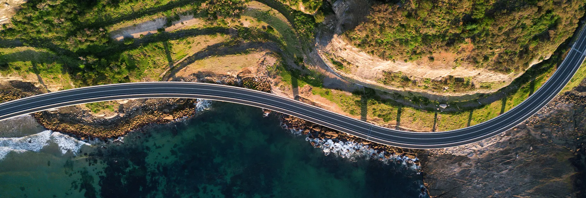 Coastal highway curving over cliffs and ocean waves below