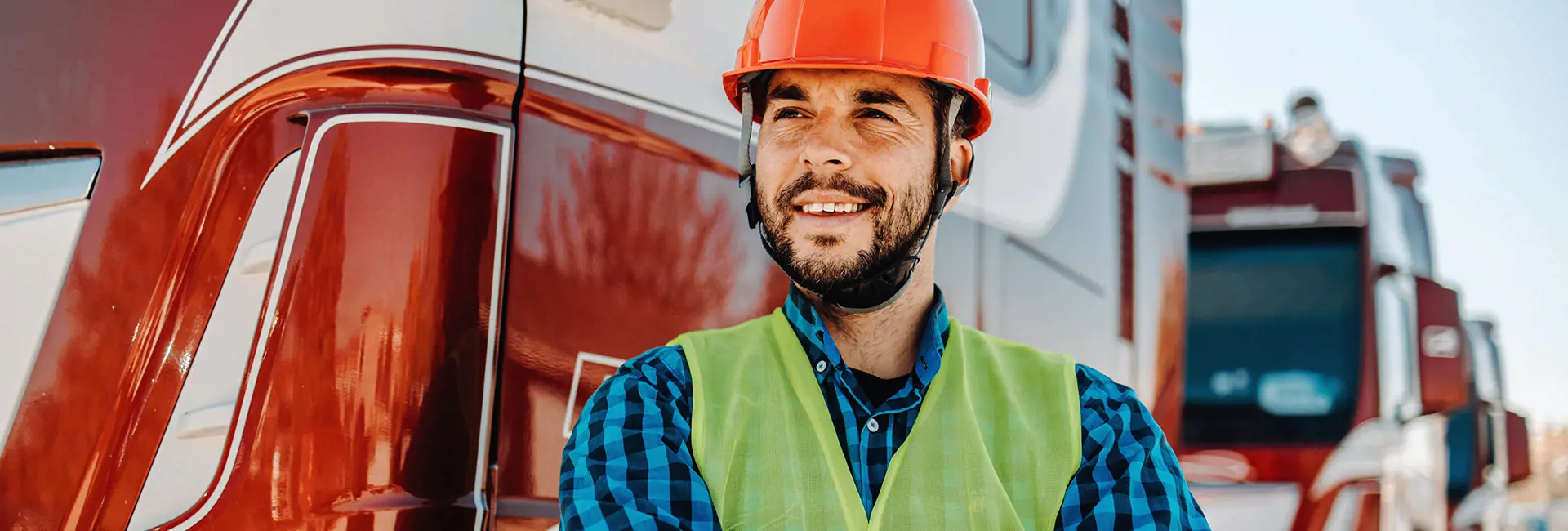 Driver smiling while standing in front of trucks parked in an outdoor setting.