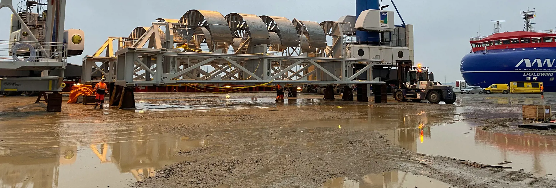 "Workers in high-visibility gear and helmets overseeing operations at a busy dockyard with cranes and ships in the background.