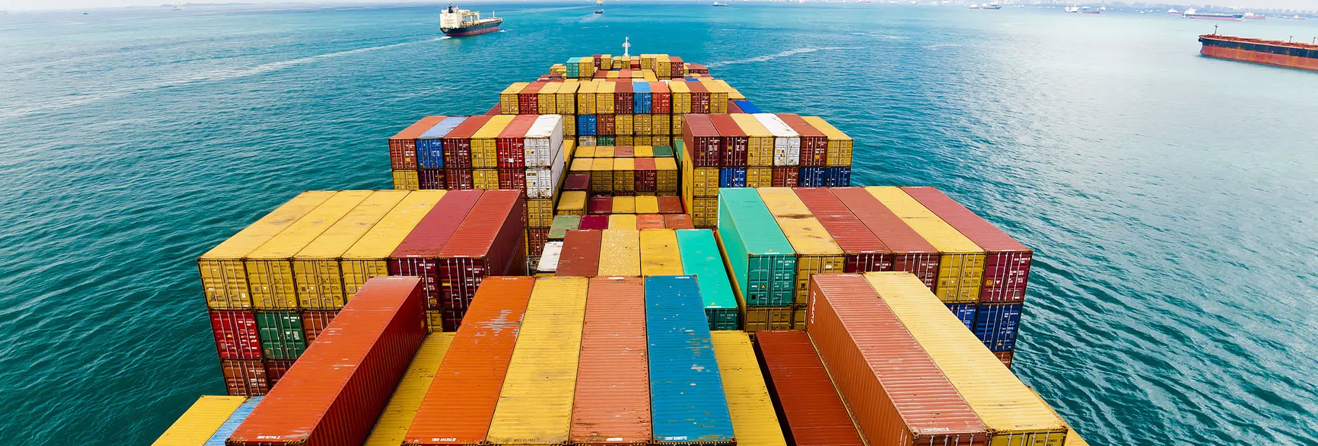 An expansive view from the deck of a cargo ship loaded with neatly stacked, multicolored shipping containers, sailing through calm blue waters. Several other vessels are visible in the distance, reflecting the collaborative and efficient nature of less-than-container load (LCL) shipping operations in ocean freight.