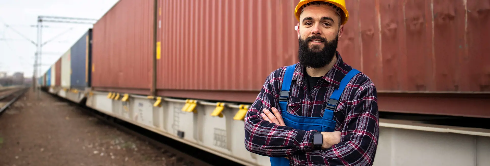 Freight train with cargo containers passing through a railway yard, with a worker standing on the tracks