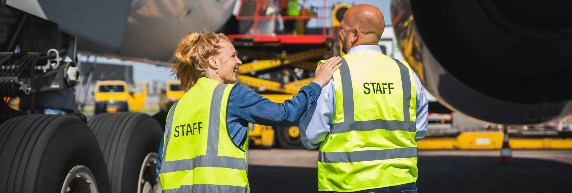 Two staff members in high-visibility vests standing near an aircraft, with one woman placing a hand on the man's shoulder