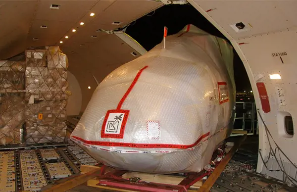 Large wrapped aircraft component secured inside a cargo plane alongside stacked freight, ready for shipment