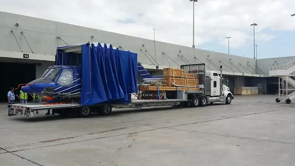 Helicopter and crates loaded on a flatbed trailer for transport at an airport cargo facility