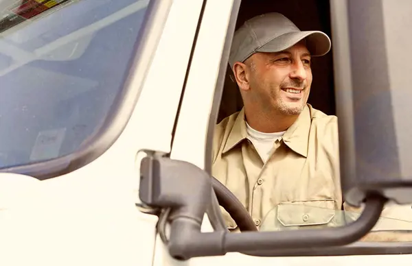 Driver in a beige shirt and cap sitting in the driver's seat of a delivery truck, with focus on the side mirror and window