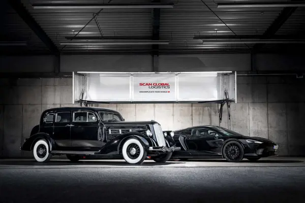 Vintage black car and modern black sports car parked in a secure warehouse under Scan Global Logistics branding