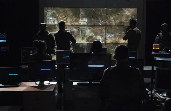 Military personnel monitoring a tactical map on a large screen in a control room