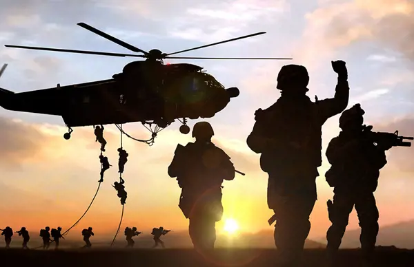 Silhouettes of soldiers and a helicopter during a military operation at sunset