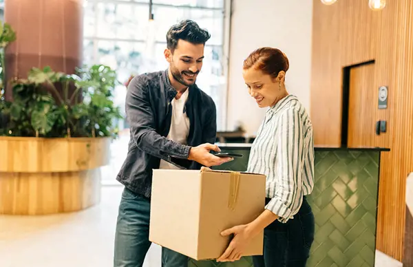 An onboard courier delivering a package to a smiling recipient in a modern lobby, with the courier holding a phone for confirmation.