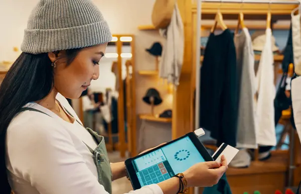 Retail worker using a tablet and scanning a card in a boutique, surrounded by clothing displays